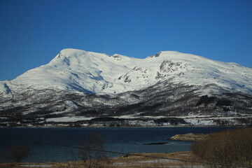 Naklejka premium Winter landscapes in Norway showcase serene snowy mountains, icy fjords, and peaceful coastal views. Capturing the beauty of snow-covered trees, quiet roads, and glowing sunsets creates a sense of cal