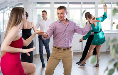 Positive woman and man dancing foxtrot in pair during group dance party