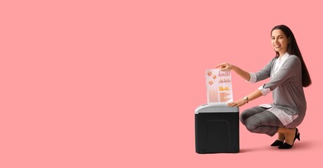 Young businesswoman destroying document by using shredder on pink background with space for text