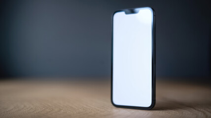 A black cell phone with a white screen sits on a wooden table. The phone is turned off and the screen is blank. Concept of emptiness and stillness, as if the phone is waiting for someone to use it
