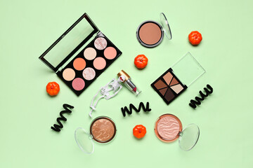 Lipstick and different decorative cosmetics with Halloween decor on green background