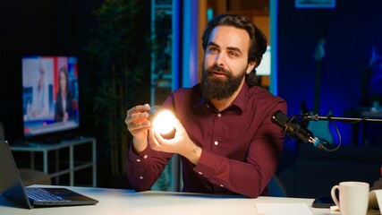 Tech guru in dimly lit apartment studio filming smart light bulb review for online streaming...