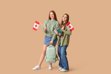 Female students with flags of Canada, notebooks and backpack on brown background