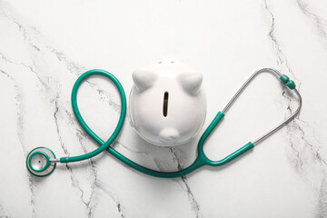 Stethoscope and piggy bank on white grunge background. Health insurance concept
