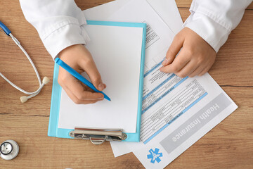 Doctor hands writing on clipboard near stethoscope and medical insurance on wooden table