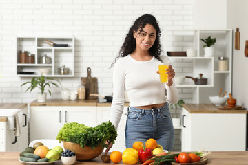 Young happy African-American woman with glass of juice, different vegetables and fruits in kitchen. Independence from Meat Day