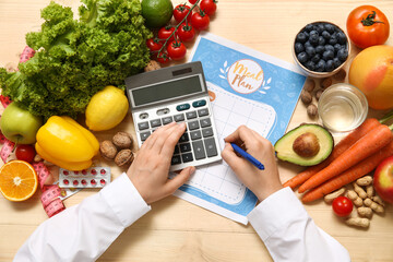 Female nutritionist writing diet plan and holding calculator near healthy food on table