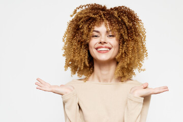 Smiling woman with curly hair expressing joy against a light background Her cheerful demeanor and open hands convey happiness and positivity Perfect for lifestyle themes