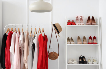 Rack of stylish clothes and shelving unit with different female shoes near white wall in wardrobe