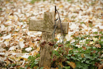 a sad forgotten grave with a weathered wooden cross in a meadow covered with autumn leaves