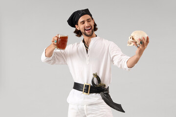 Young pirate with rum and skull on light background