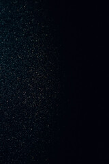 Dark minimalistic texture with a light gradient of bluish and yellowish speckles, resembling scattered snow or dust on a smooth, glass surface. Abstract, atmospheric background.

