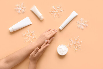 Female hands with snowflakes, jar and tubes of cosmetic cream and snowflakes on beige background