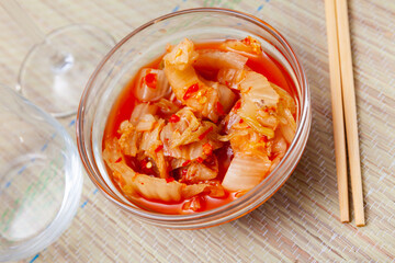 Kimchi cabbage in a bowl with chopsticks for eating on wooden background, top view, Korean food