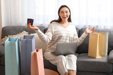 Young woman with credit card, laptop and shopping bag at home. Black Friday sale