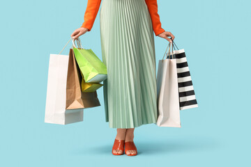 Beautiful young woman with shopping bags on blue background, closeup