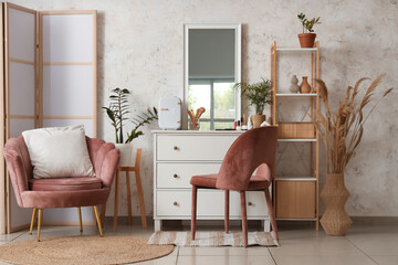 Interior of stylish makeup room with mirror, drawers and armchair