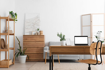 Blank laptop with frame and plant on programmer's desk in living room