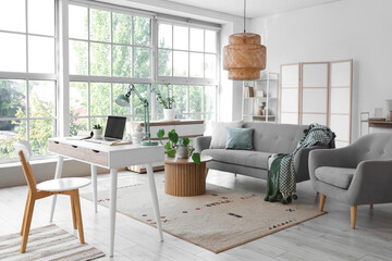 Interior of light living room with programmer's workplace, sofa and armchair
