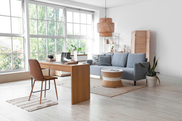 Interior of light living room with programmer's workplace, sofa and folding screen