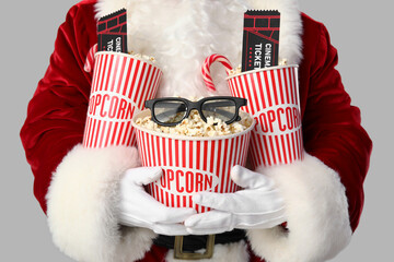 Santa Claus with buckets of popcorn, cinema tickets, candy canes and 3D glasses on grey background....