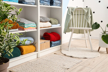 Shelving unit with clothes and chair in dressing room. Closeup