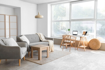 Interior of light living room with workplace, sofa and armchair