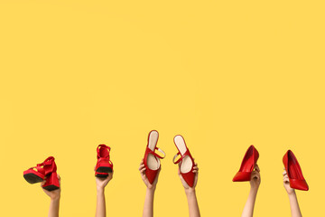Female hands with stylish red high heeled shoes on yellow background