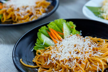 A delicious plate of pasta topped with grated cheese and fresh vegetables on the side.