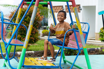 A happy boy enjoys playing on a colorful swing at a playground.