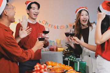 Group of young Asian man and women as friends having fun at a New Year's celebration, holding gift boxes standing by Christmas tree decoration, midnight countdown Party at home with holiday season.