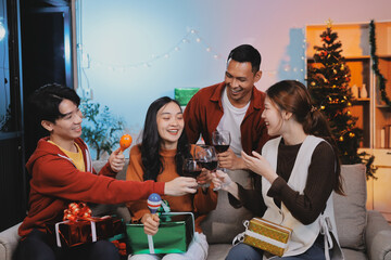 Group of young Asian man and women as friends having fun at a New Year's celebration, holding gift boxes standing by Christmas tree decoration, midnight countdown Party at home with holiday season.