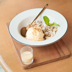 Apple Crumble. A top view of apple crumble with vanilla sauce and ice cream. Selective focus on Vanilla ice cream. Served on the wooden table.