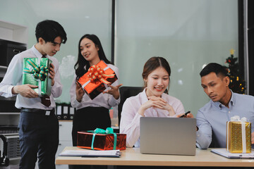 full length view of a group of business team wearing red Santa hat and exchange gift box together in the office for Christmas.