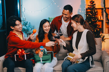 Group of young Asian man and women as friends having fun at a New Year's celebration, holding gift boxes standing by Christmas tree decoration, midnight countdown Party at home with holiday season.