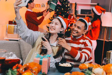 Group of happy Asian friends celebrating Christmas and decorate the Christmas tree indoors. Beauty woman with Christmas Gifts. New Year party. Woman hands decorate Christmas tree red ball, bauble.