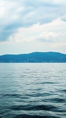 Obraz premium A serene view of calm waters reflecting a cloudy sky and distant hills.