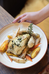 Hand serving whole roasted mini chicken with vegetables and herbs on plate