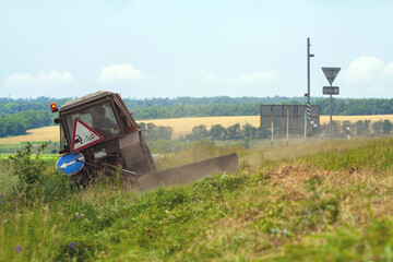 Tractor with a mechanical mower mowing grass on the side of the asphalt road