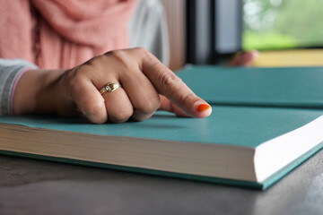 A hand points at an open book on a table, evoking calm and concentration in soft daylight
