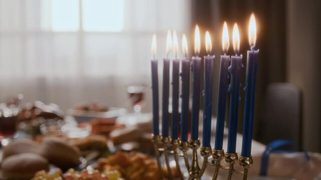 Close-up view of Hanukkah menorah with lit blue candles on festive dinner table full of traditional Jewish foods