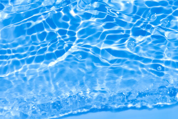 Blue water with ripples on the surface. Defocus blurred transparent blue colored clear calm water surface texture with splashes and bubbles. Water waves with shining pattern texture background.
