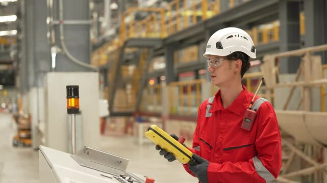 An engineer in red coveralls and a hard hat speaks into a radio while working in a train maintenance depot.