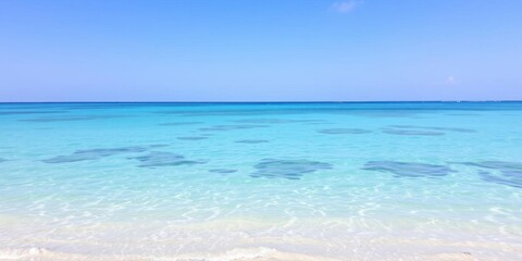 Obraz premium A serene ocean background showcasing crystal clear blue water, a sandy beach, and a cloudless sky, relaxation, tropical
