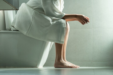 Woman sitting on the toilet bowl in the bathroom. She has stomach ache. Poor digestive system....