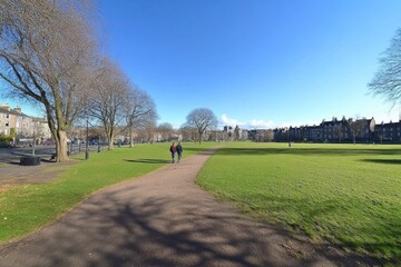 Obraz premium A serene park scene featuring two people walking on a path under a clear blue sky.