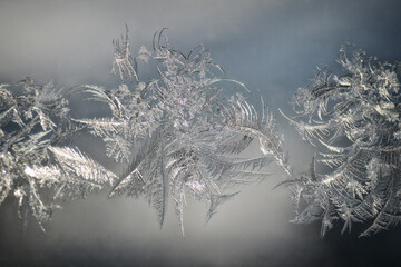 Delicate frost snowflake patterns resembling feathers have formed on a window pane, creating a...