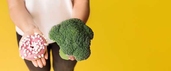 Healthy Lifestyle. Broccoli And Junk Food Donut In Hands Of Unrecognizable Woman Over Yellow...
