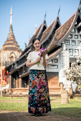 Obraz premium A charming Asian woman with a temple in the background, admiring a flower bouquet in her hand.