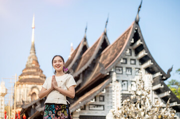 A beautiful Asian woman stands outdoors in a praying posture, with a temple in the background.